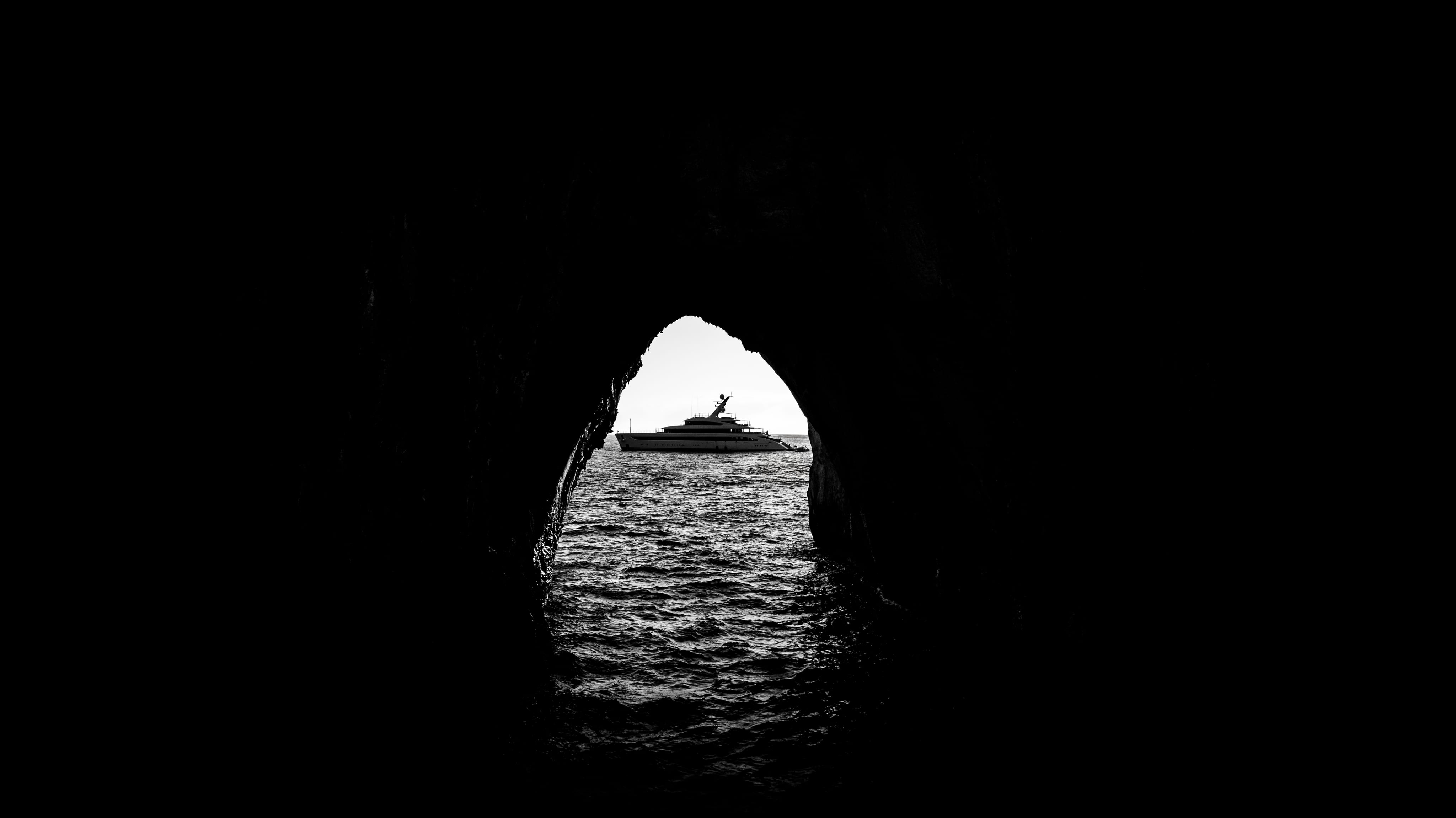 Superyacht framed through a sea cave at golden hour.
